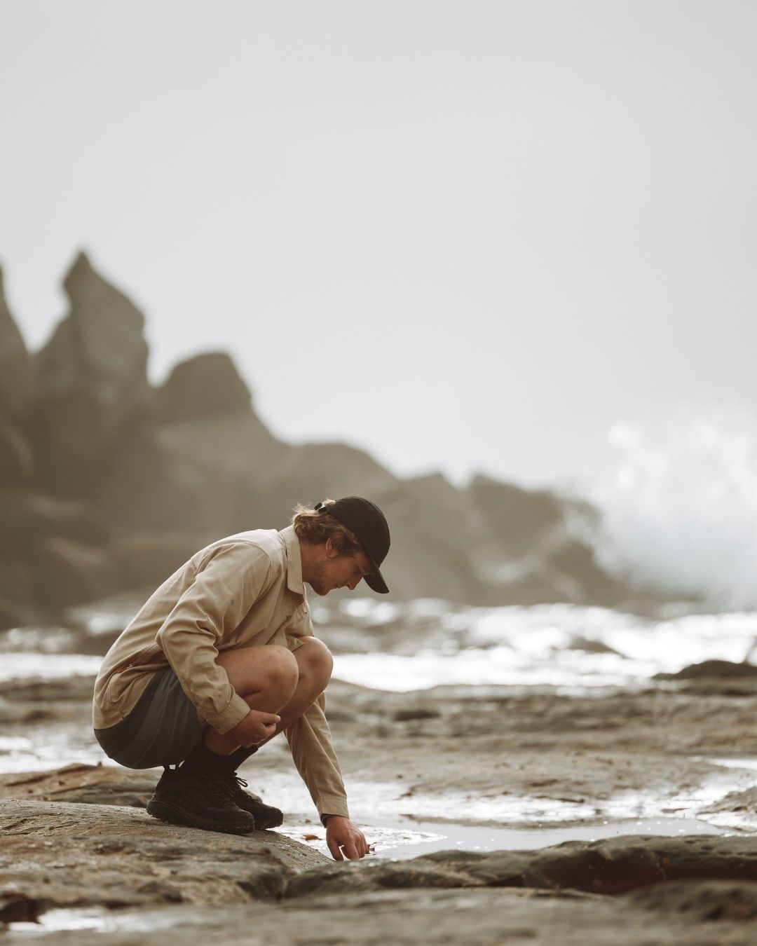 Man crouching on wet shoreline rocks wearing the XTM Hakea cap in Black
