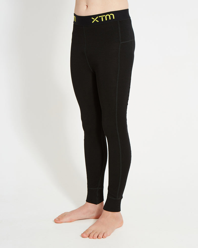 XTM Kids Alpine230 Merino Thermal Pants in Black, three-quarter view showing the flatlock seams
