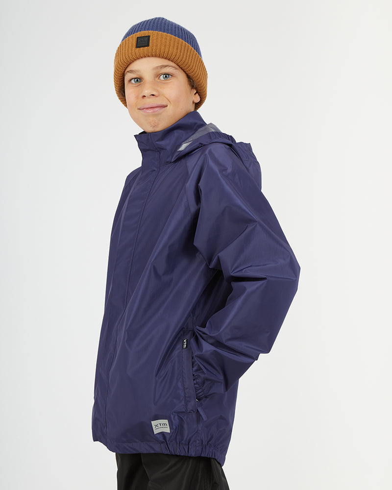 Boy in the XTM Kids Stash 2L rain jacket in Patriot Blue, hand in a side zip pocket