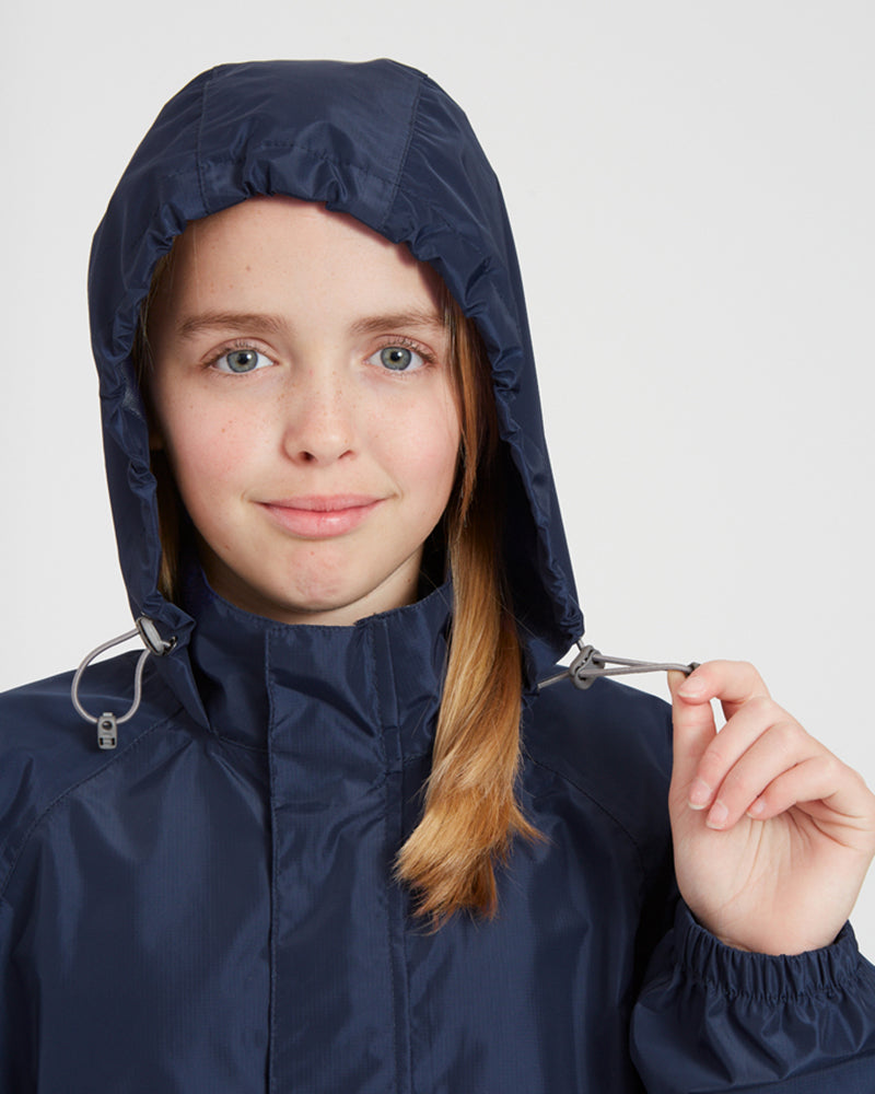 Girl tightening the hood toggle on the XTM Kids Stash 2L rain jacket in Patriot Blue
