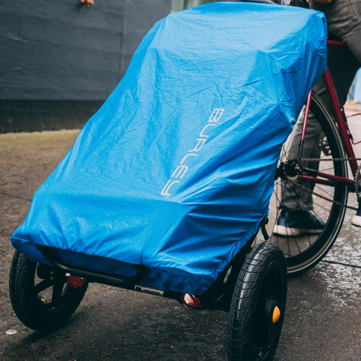 Blue Burley Travoy Rain Cover with reflective Burley logo over a loaded Travoy hitched to a bike on wet road