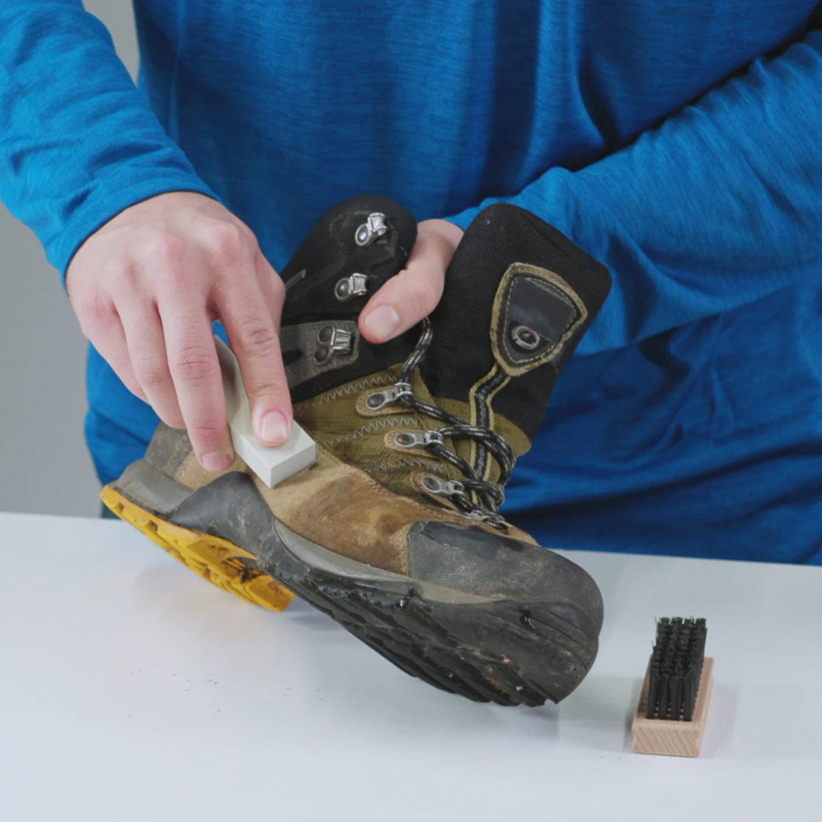 Rubbing a white block over the scuffed toe of a brown leather hiking boot