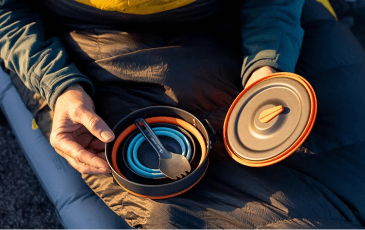 Hands nesting the collapsed blue cup and spork inside the Frontier UL pot on a sleeping bag