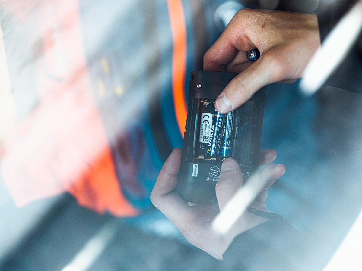 Hands fitting AAA batteries into the back of a Mammut Barryvox avalanche beacon