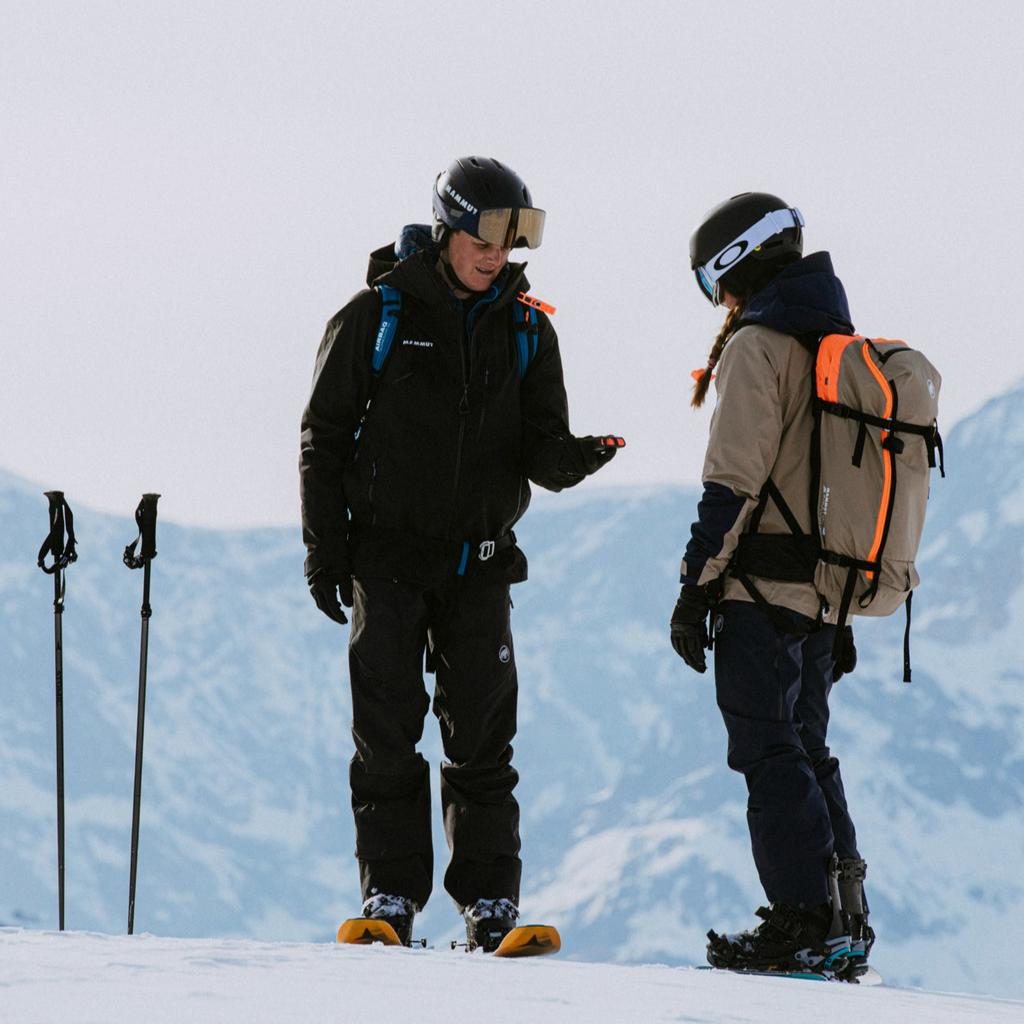Two ski tourers facing each other on a snowy ridge doing a beacon check before setting off