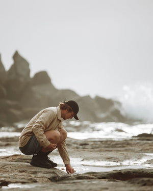 Man crouching on wet shoreline rocks wearing the XTM Hakea cap in Black