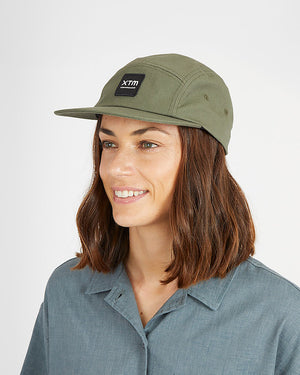 Woman wearing the XTM Hakea organic cotton cap in Thyme, an olive green 5-panel cap with XTM patch