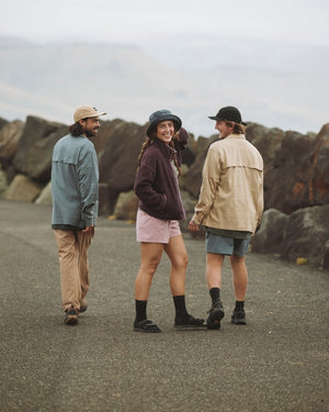 Three friends walking by a rocky sea wall, the woman in the Indigo XTM Sundew bucket hat