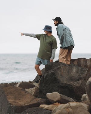 Man in the Indigo XTM Sundew bucket hat pointing out to sea from coastal rocks