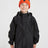 Boy wearing the XTM Kids Stash 2L rain jacket in Black, front view, zipped with hood rolled away