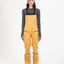 Woman wearing the XTM Stellar snow bib pant in Mustard with ski boots, front view