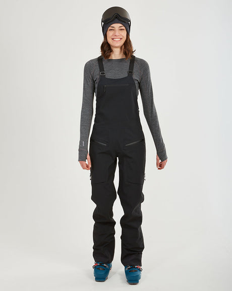 Woman wearing the black XTM Stellar 2.0 hardshell bib pant with ski boots, front view