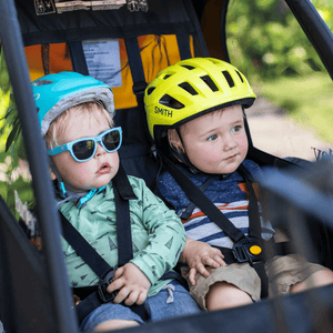 Two toddlers in helmets buckled into the harnesses of a Burley Bee Double