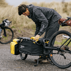 Rider packing a yellow dry bag into a Burley Coho XC parked on its kickstand behind his bike