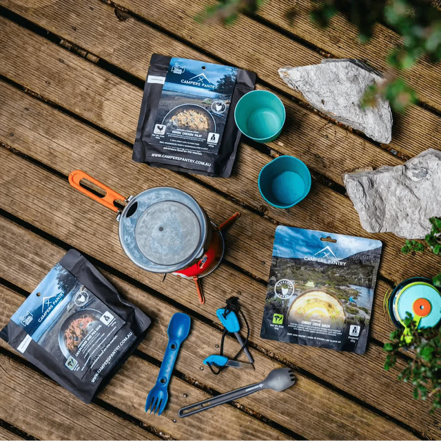 Campers Pantry pouches, a stove, mugs and a spork laid out on a timber deck