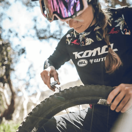 Mountain biker crouched beside a tubeless tyre using a Lezyne plug tool on the trail