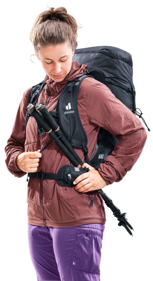 Woman stowing trekking poles in the quick-release holders on the Deuter Speed Lite Pro 28 SL